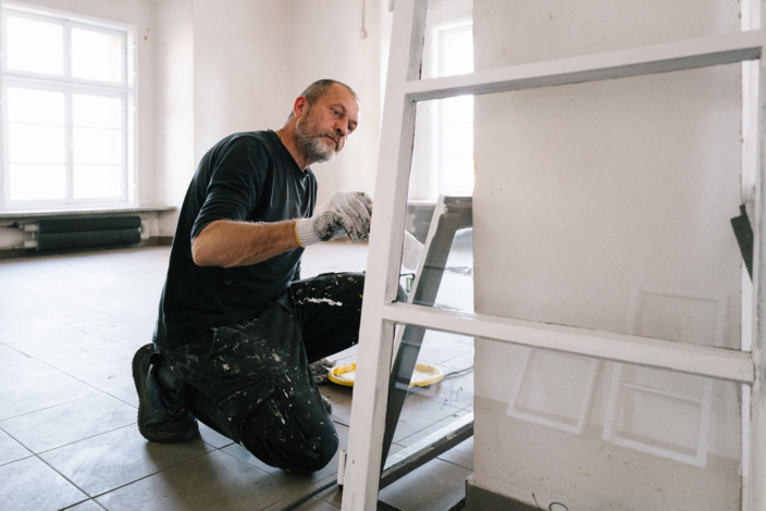 Maler streicht Fensterrahmen in einer Wohnung, die renoviert wird.