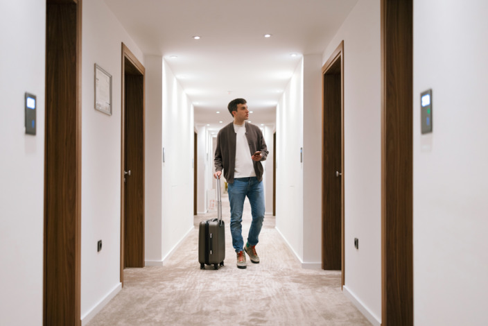 Mann läuft mit seinem Koffer durch einen Hotelflur.