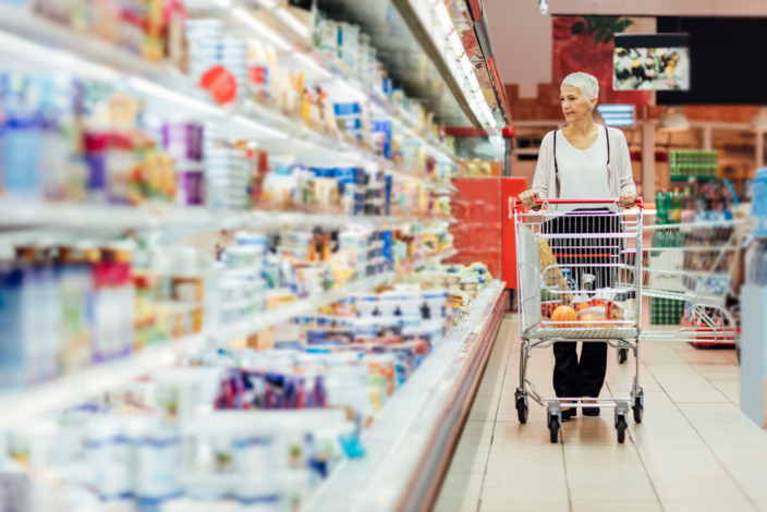 Frau fährt mit einem Einkaufswagen an einem Supermarktregal entlang