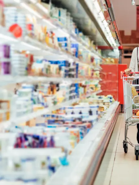 Frau fährt mit einem Einkaufswagen an einem Supermarktregal entlang