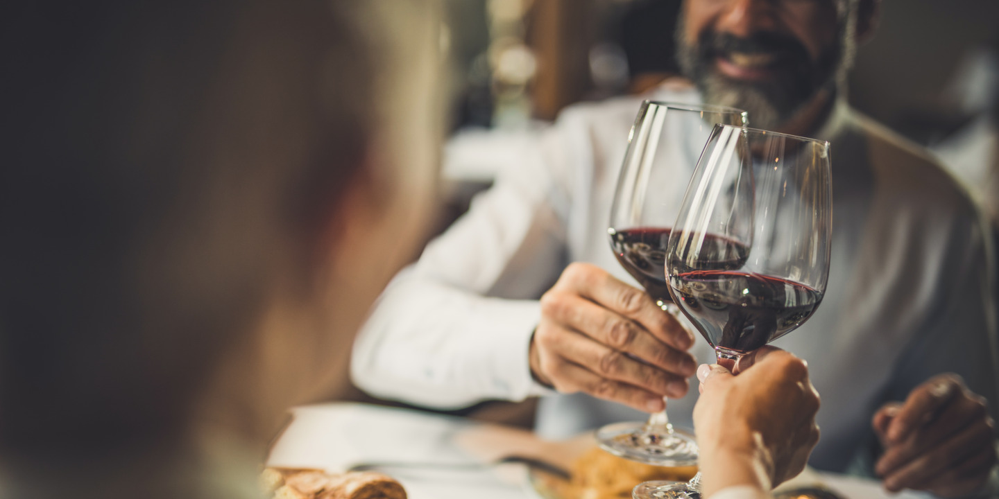 Zwei Menschen sitzen beim Essen und stoßen mit Rotwein an