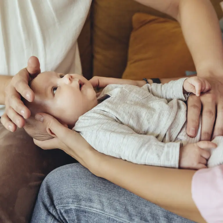 Mutter hält ihr Baby auf den Knien während eine Hebamme es untersucht