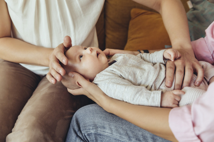 Mutter hält ihr Baby auf den Knien während eine Hebamme es untersucht