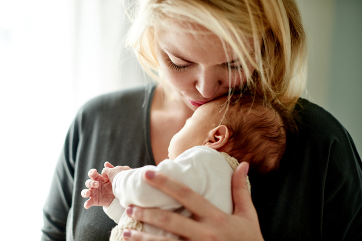 Mutter hält ihr Baby auf dem Arm und küsst es auf die Stirn