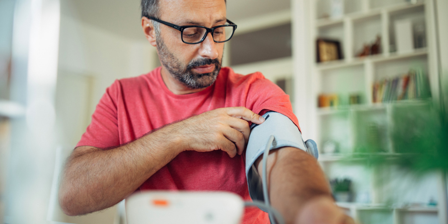 Mann mittleren Alters mit Brille misst Blutdruck am Arm. 