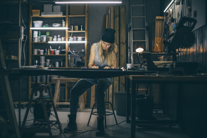 Frau sitzt zufrieden lächelnd und versunken in ihre Arbeit am Schreibtisch in einer Werkstatt - Symbolbild für Stressresistenz