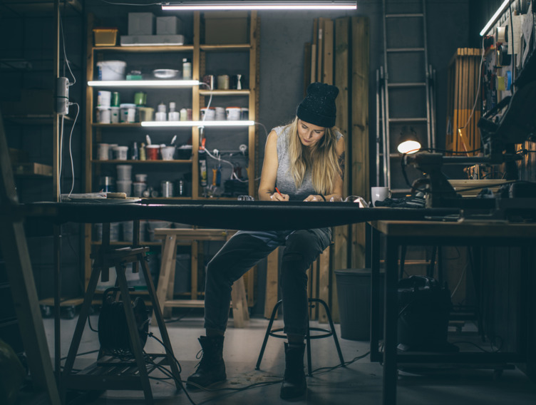 Frau sitzt zufrieden lächelnd und versunken in ihre Arbeit am Schreibtisch in einer Werkstatt - Symbolbild für Stressresistenz