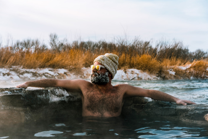 Mann mit Sonnenbrille und rauhreifbedeckter Strickmütze beim Eisbaden