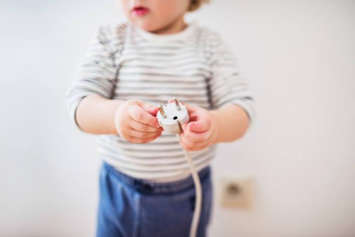 Kleinkind hält den Stecker eines Elektrogerätes in der Hand