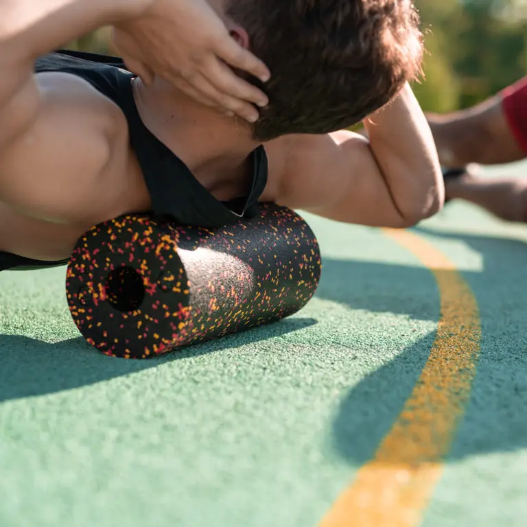 Mann in Sportkleidung rollt mit der Schulterpartie über die Faszienrolle