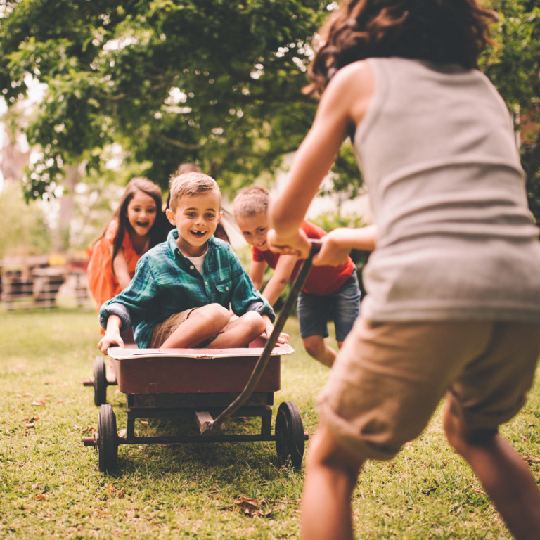 Vier Kinder spielen mit einem Bollerwagen