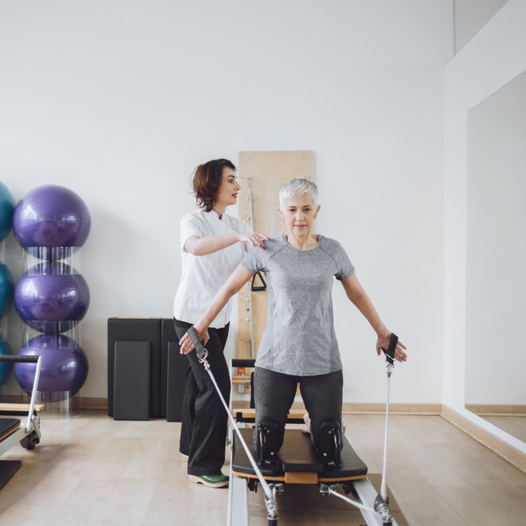 ältere Frau absolviert Pilatesübungen mit einer Trainerin
