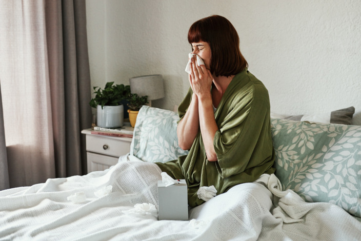 Frau sitzt auf dem Bett und niest in ein Taschentuch