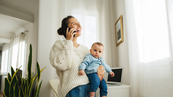 Mutter mit Baby auf dem Arm telefoniert mit dem Handy