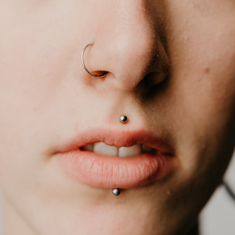 Gesicht einer jungen Frau, die ein Nasenpiercing und zwei Lippenpiercings trägt