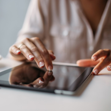 Frau sitzt mit Kaffeetasse und Tablet am Tisch