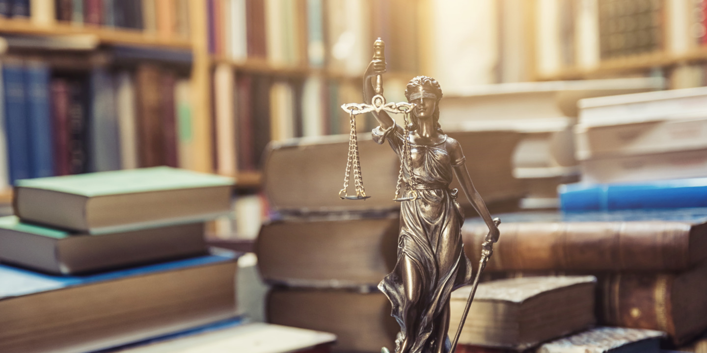 Justitia-Statue steht vor Stapeln von Büchern