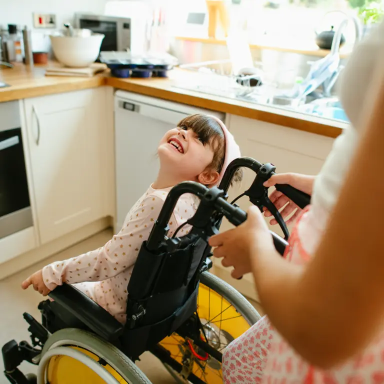 Frau schiebt ein kleines Mädchen im Rollstuhl durch eine Küche
