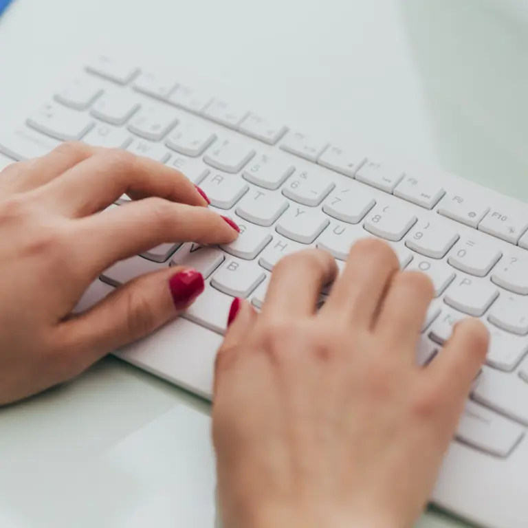 Zwei Hände mit rot lackierten Fingernägeln tippen auf einer Tastatur.