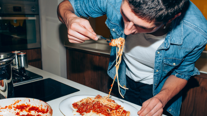 Student isst Spaghetti mit Tomatensoße im Stehen