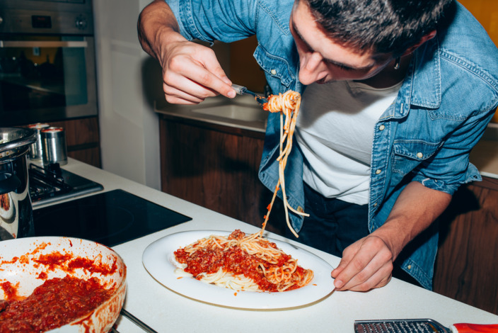 Student isst Spaghetti mit Tomatensoße im Stehen