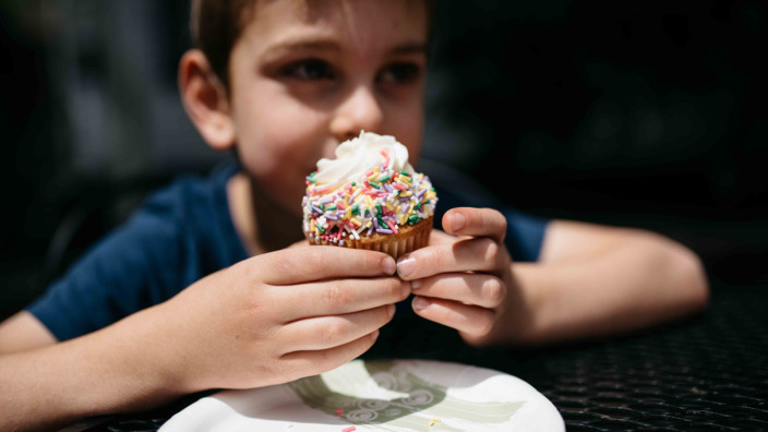 Junge hält einen stark gezuckerten Muffin in seinen Händen