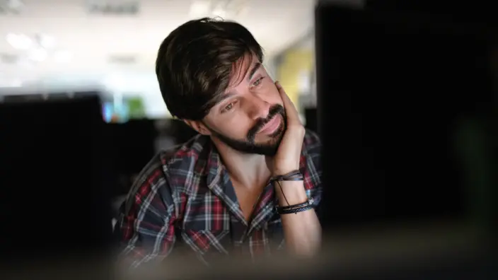 Mann sitzt nachdenklich vor seinem Rechner – Symbolbild für Kritikfähigkeit