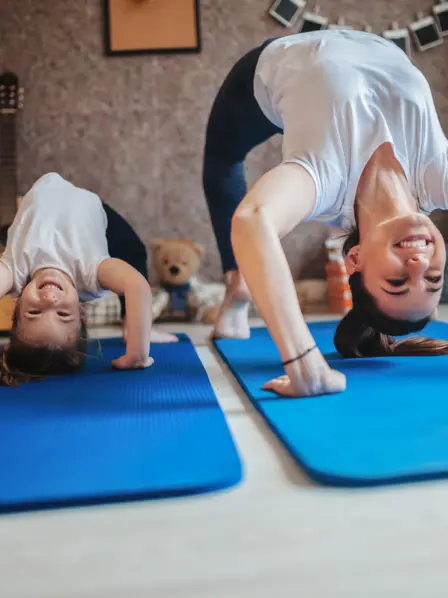 Mutter und ihre kleine Tochter machen eine Brücke auf einer Yoga-Matte