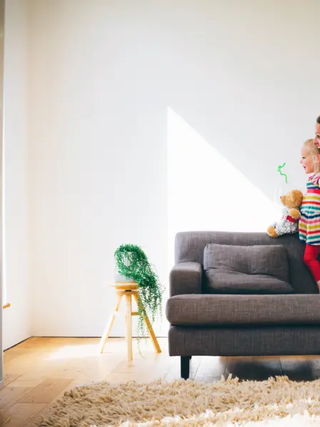 Mutter und Tochter sitzen auf der Rückenlehne eines grauen Sofas und spielen Flugzeug