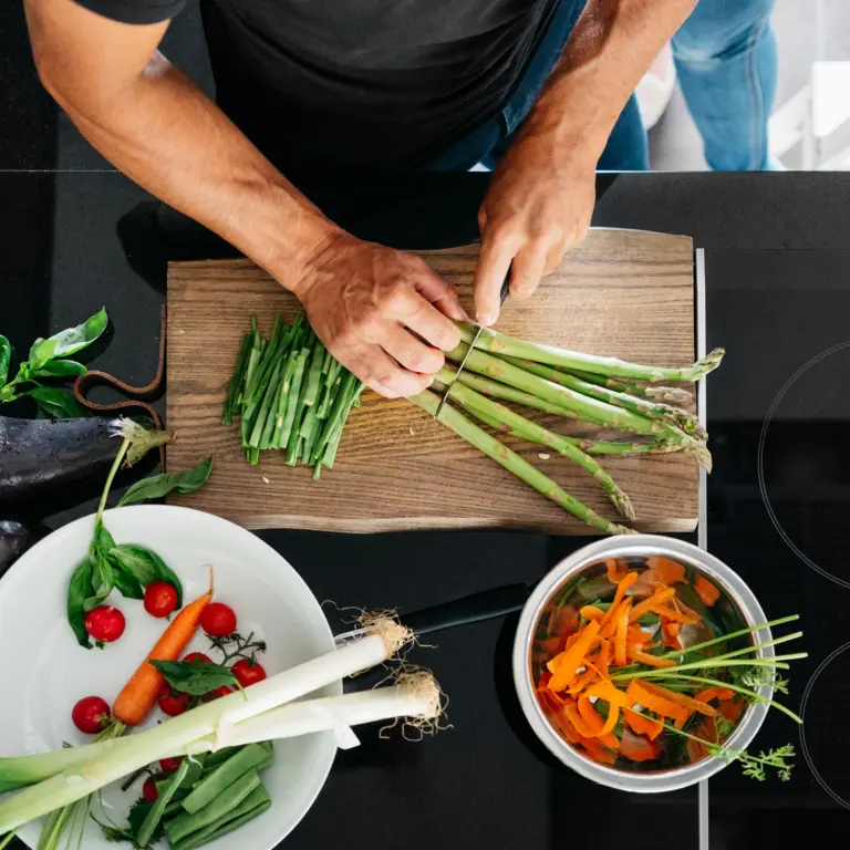 Mann schneidet in der Küche Gemüse auf einem Holzbrett.