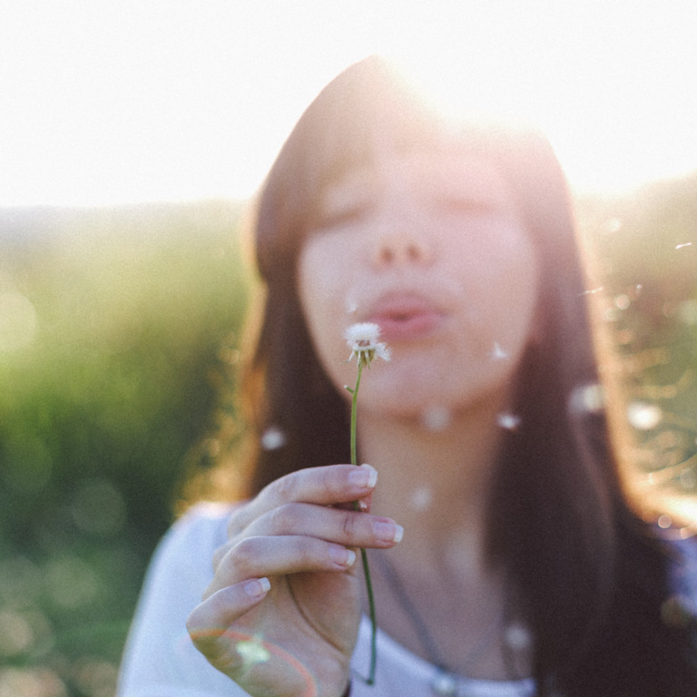 Frau pustet auf eine Pusteblume