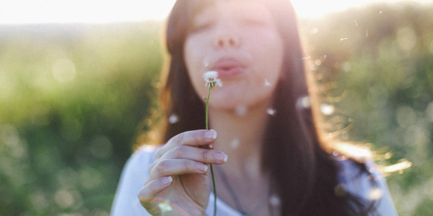 Frau pustet auf eine Pusteblume