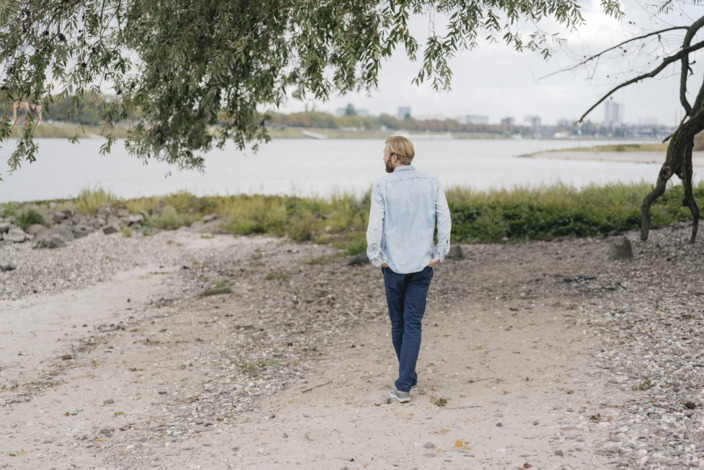 junger Mann geht gedankenversunken am Ufer eines Flusses entlang