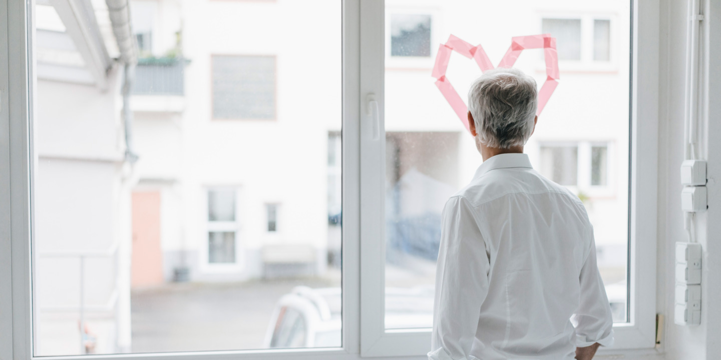 Mann schaut nachdenklich aus einem Fenster auf dem ein Herz klebt