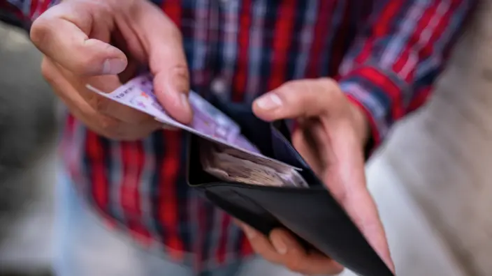Mann im Flanell-Hemd nimmt Geld aus seiner Geldbörse.