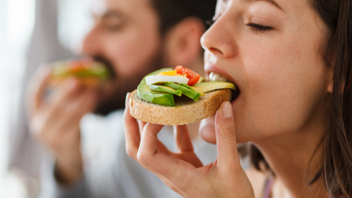 Eine junge Frau beisst in ein Brot mit Avocado