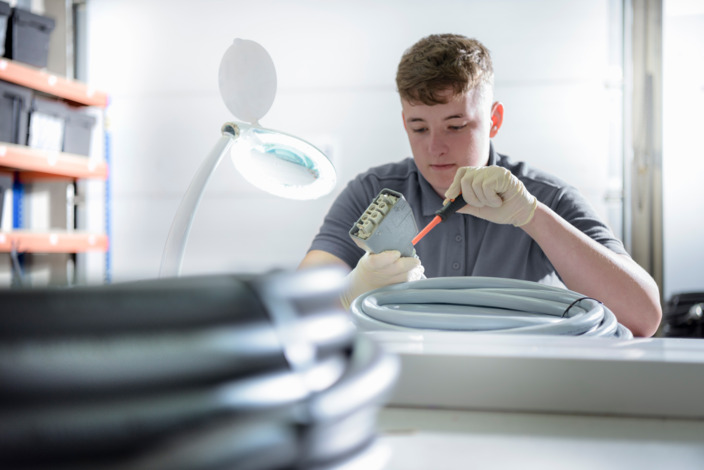 Auszubildener sitzt in der Werkstatt und schraubt ein Kabel an