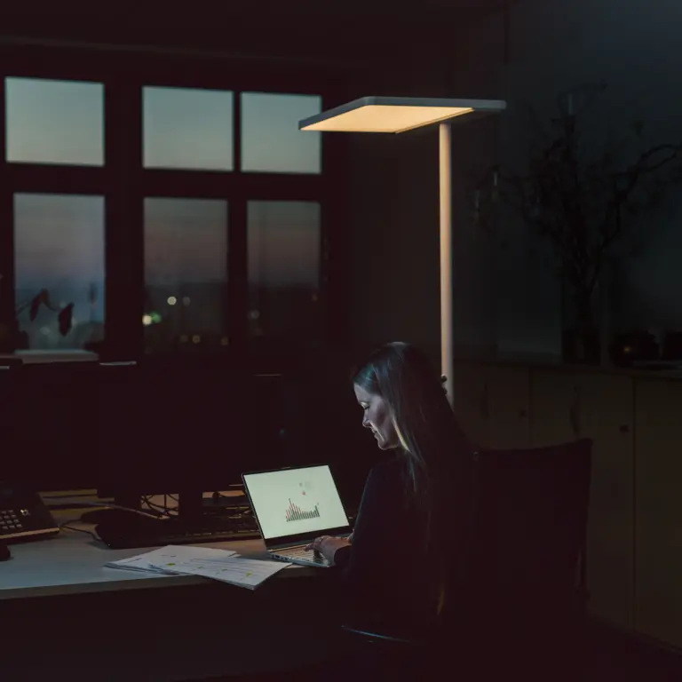 Frau, die abends im Büro am Laptop sitzt. 