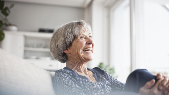 Seniorin sitzt gut gelaunt auf ihrer Couch