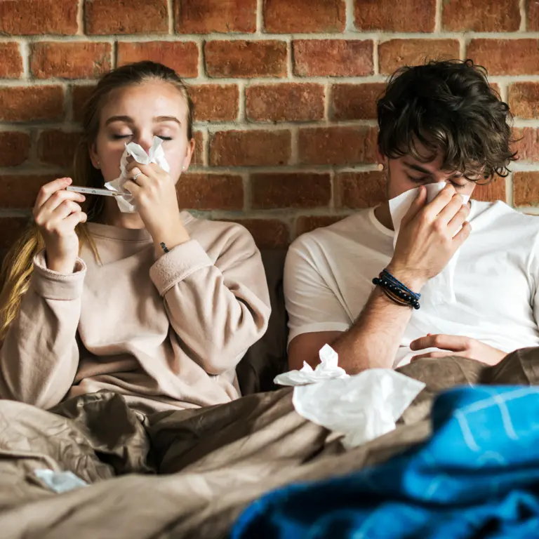 Paar sitzt erkältet im Bett und benutzt Taschentücher