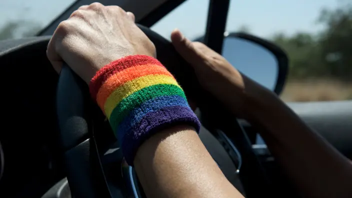 Person mit Armband in Regenbogen-Farben fährt Auto.