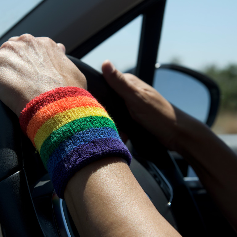 Person mit Regenbogen-Armband fährt Auto. 