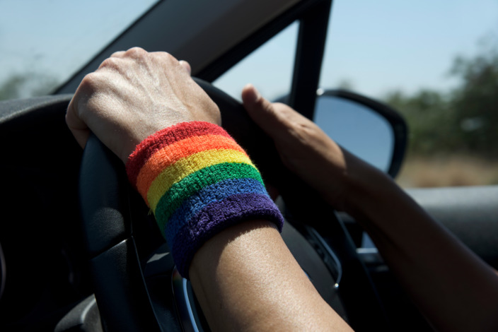 Person mit Armband in Regenbogen-Farben fährt Auto.