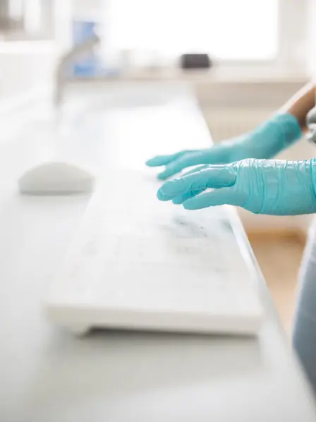 Hände mit medizinischen Handschuhen tippen auf Tastatur