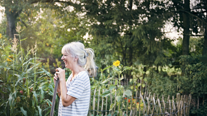 Frau mit einer Koronaren Herzkrankheit steht lachend in ihrem Garten