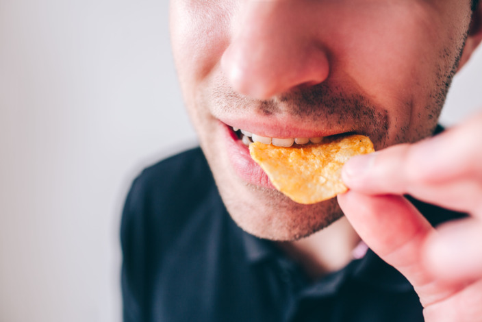 Mann steckt sich Kartoffelchips in den Mund.