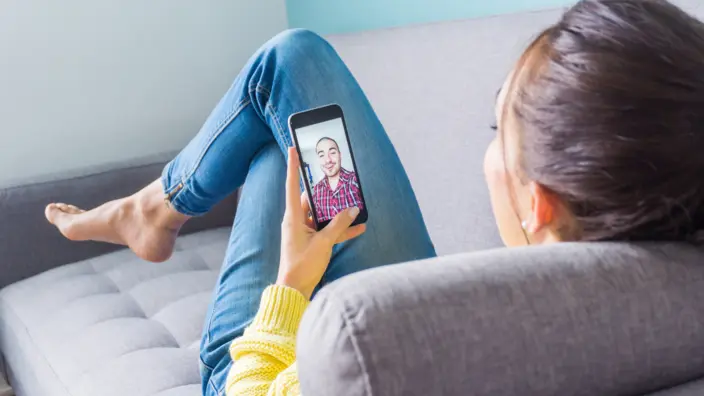 Frau liegt auf dem Sofa und videochattet mit einem Mann.