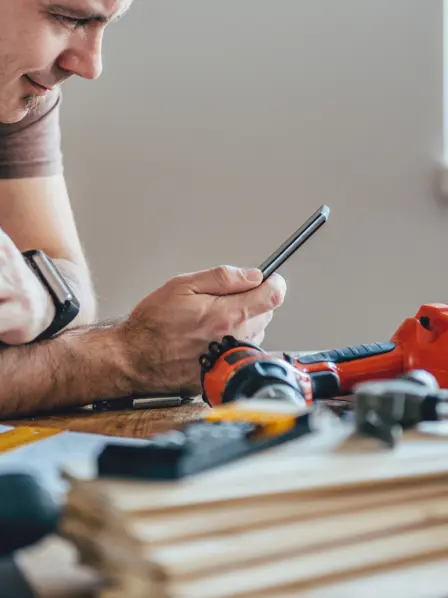Handwerker schaut auf sein Handy und trinkt Kaffee.