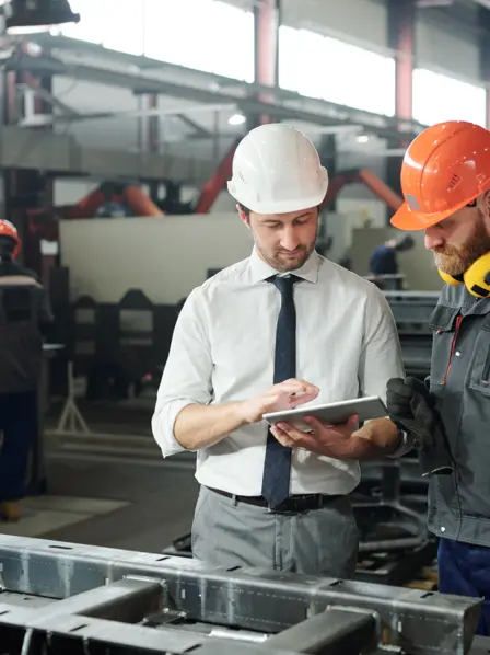 Zwei Arbeiter stehen in Werkshalle und schauen auf ein Tablet.
