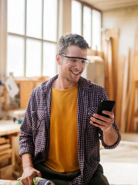 Handwerker steht in Werkstatt und schaut auf sein Handy